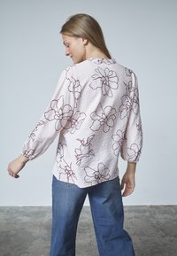 Lyserød blomsterbluse med burgunder kanter, lange ærmer med elastiske manchetter og en afslappet pasform. Sammen med blå brede bukser.