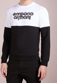 Black and white cotton sweatshirt with long sleeves and a round neckline, featuring a prominent embroidered "Emporio Armani" logo on the front.