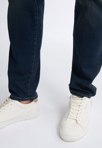 Ležérní tmavě modré džíny kombinované s bílými teniskami s hladkou kůží, plochými tkaničkami a jemným béžovým akcentem na patě.