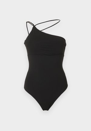 Maillot de bain une pièce noir avec encolure asymétrique et deux fines bretelles sur fond blanc.
