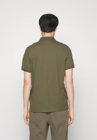Polo shirt vert olive à manches courtes avec un tissu texturé, ourlet droit et poignets repliés, porté avec un pantalon vert assorti.