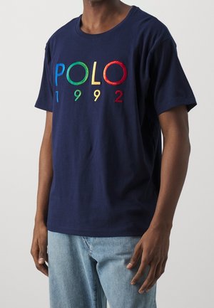 Marineblaue Baumwoll-T-Shirt mit "POLO 1992" in mehrfarbig gesticktem Text. Mit kurzen Ärmeln und Rundhalsausschnitt.