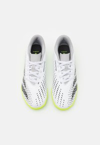 Scarpe da calcio bianche con accenti neri e gialli, dotate di un upper testurizzato, finitura liscia e lacci. Progettate per prestazioni e aderenza.