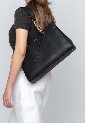 Black leather tote bag with a textured surface, gold chain strap accents, rectangular shape, and metal feet on the base.