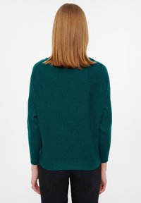 Teal gebreide trui met een relaxte pasvorm, lange mouwen, ribbeltextuur en een afgeronde zoom, gecombineerd met zwarte broek.