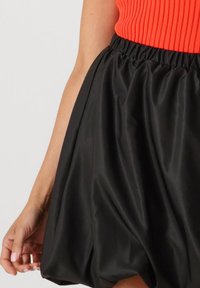 Zwarte satijnen minirok met een elastische tailleband, met een volumineus ontwerp en een gladde oppervlakte, gecombineerd met een oranje ribbeltop.
