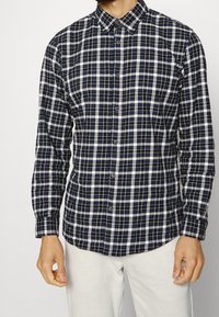 Button-up shirt in navy and white plaid pattern, made of cotton, featuring a classic collar and long sleeves.
