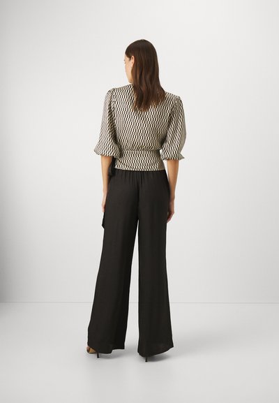 Lett, mønstrete bluse med puffermet er parret med vide, svarte bukser, som har en avslappet passform og glatt tekstur.