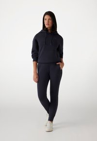 Sweat à capuche marine avec poche avant et leggings ajustés marine. Les deux sont en tissu doux, avec un branding subtil le long de la jambe.