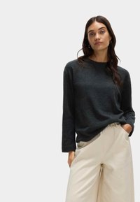 Ciemnoszara, długosleeve sweter o luźnym kroju i okrągłym dekolcie, zestawiony z kremowymi, szerokimi spodniami. Miękka faktura, minimalizm w designie.