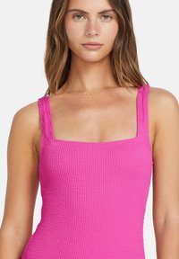 Haut rose vif à col carré en tissu texturé avec des bretelles larges, mettant en avant un design ajusté. Présente un motif côtelé pour plus de détails.