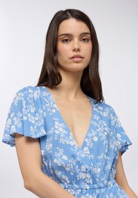 Abito azzurro chiaro con stampa floreale bianca, scollo a V, maniche corte a volant e vita elastica per una vestibilità comoda.