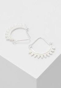 Silverfärgade hoopörhängen med en pärldesign och en texturerad mönstring som skapar en distinkt, halvcirkelform.