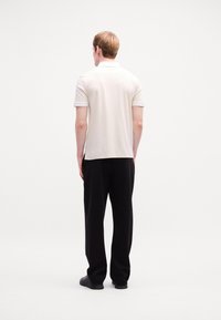 Polo shirt de culoare bej deschis, cu mâneci scurte și accente ribelate, asortat cu pantaloni negri, lejeri. Design simplu și curat.
