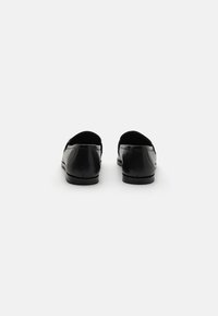 Mocassins en cuir noir avec une finition lisse, des bouts arrondis et des talons bas. Présentent un design à enfiler et des détails de couture minimalistes.