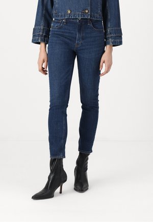Dark blue denim jeans with a slim fit, high waist, and subtle stitching details, paired with black pointed-toe ankle boots.