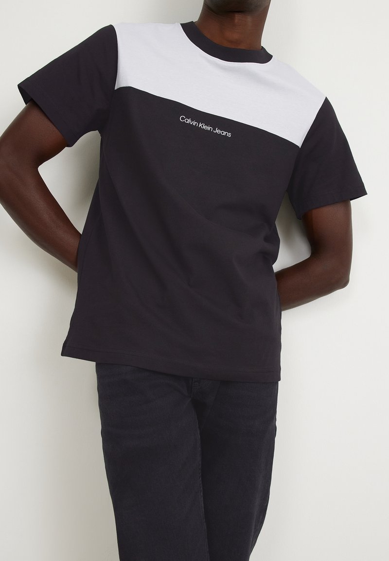 Camiseta bloqueada en negro y blanco, de cuello redondo, de mangas cortas, con el logo "Calvin Klein Jeans" en blanco en el pecho. Material de algodón.