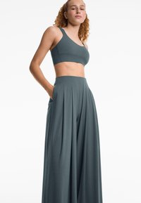 Lichtgewicht, donkergroene, rekbare stoffen twee-delige outfit bestaande uit een cropped top en wijde broek met plooien en zijzakken.