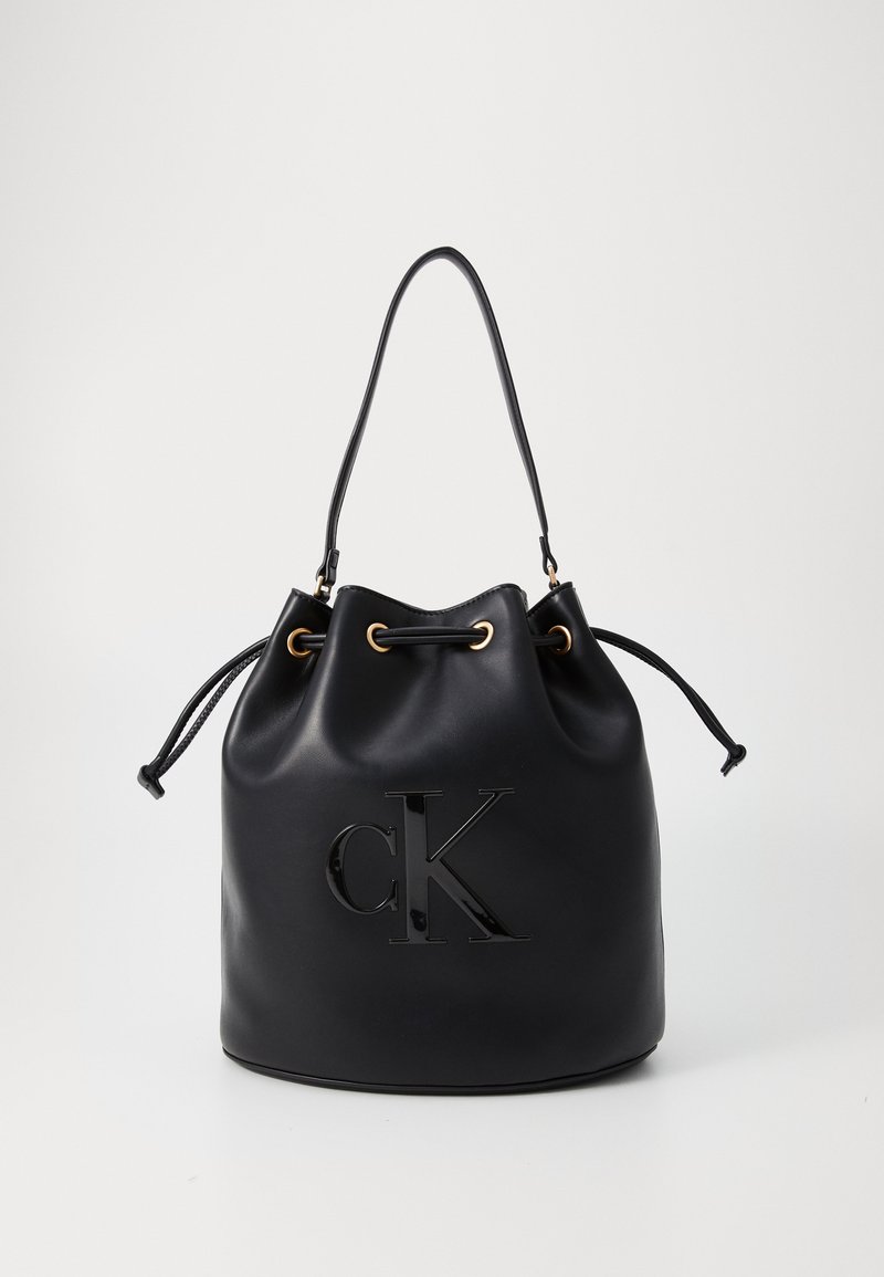 Schwarze Leder-Eimer-Tasche mit Kordelzugverschluss, ausgestattet mit einem glänzenden "CK"-Logo auf der Vorderseite und goldfarbenen Hardware-Akzenten.
