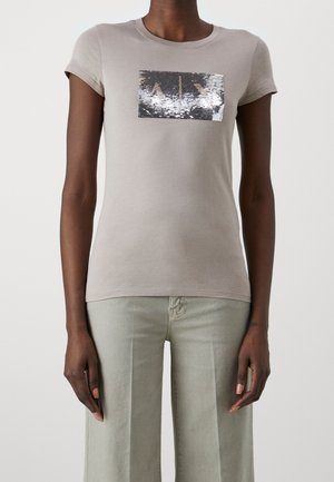 Kurzärmeliges, helltaupefarbenes T-Shirt mit einem rechteckigen silbernen Paillettenmotiv auf der Vorderseite. Weiches Baumwollmaterial, figurbetonte Form.