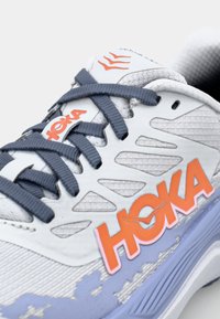 Hoka løpesko i hvit og lys lilla, med mesh-overdel, oransje logo og marineblå snørebånd. Merkeverdige utskjæringer for ventilasjon.