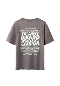 T-shirt gris à manches courtes avec un texte graphique blanc, présentant des phrases comme "Édition Limitée" et "Né pour les Rues", dans différentes polices.