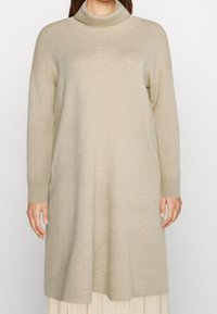 Béžové rolákové šaty vyrobené z měkké pleteniny, s dlouhými rukávy a volným střihem dosahujícím do poloviny stehna. Minimalistický design.