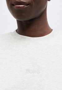 Κοντινό πλάνο ατόμου που φορά ανοιχτό γκρι φούτερ με ανάγλυφο λογότυπο "BORG" στο στήθος, εμφανίζοντας το κάτω μέρος του προσώπου, τον λαιμό και το άνω μέρος του κορμού.