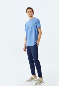 Blårandig t-shirt med kort ärm, parat med marinblå byxor med smal passform och ljusgrå sneakers med svarta accenter. Enkel, avslappnad design.