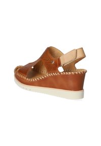 Sandalo con zeppa in pelle marrone, caratterizzato da un design a ritagli e bordi intrecciati. Dotato di una cinghia alla caviglia e una suola in gomma bianca a contrasto.
