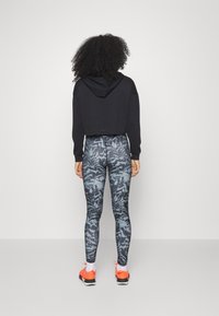Czarny krótkie bluza z długim rękawem, sparowana z dopasowanymi legginsami w niebieski wzór kwiatowy, noszona z jaskrawymi pomarańczowymi butami sportowymi.