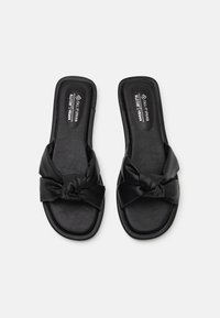 Sandales à glisser véganes noires avec un détail de nœud sur le dessus, présentant une surface synthétique lisse et une semelle intérieure rembourrée.