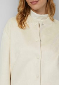 Cremefarbene Jacke mit weicher Textur, geripptem Kragen und fünf Druckknöpfen. Verfügt über ein schlichtes Design, geeignet für legere Trageweise.