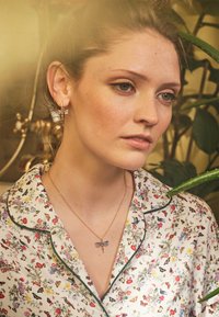 Ziedu naktskreklis ar zaļajiem maliņām. Zelta kaklarota ar pūces piekariņu. Stilizēts ar mazām auskaru riņķī. Fons satur augus.