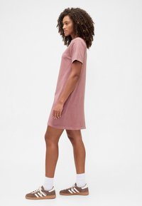 Sukienka z bawełnianej koszulki w jasnoróżowym kolorze, z krótkimi rękawami, luźnym krojem, sięgająca do kolan z prostym dołem. W połączeniu z brązowymi tenisówkami i białymi skarpetkami.