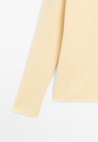 Pullover lavorato a maglia giallo chiaro con una finitura testurizzata, caratterizzato da un orlo dritto e maniche lunghe. I bordi sono rifiniti con un margine pulito.