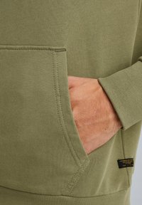 Olive green sweatshirt featuring ribbed cuffs and hem, large front pocket, and a small black label on the lower left side.