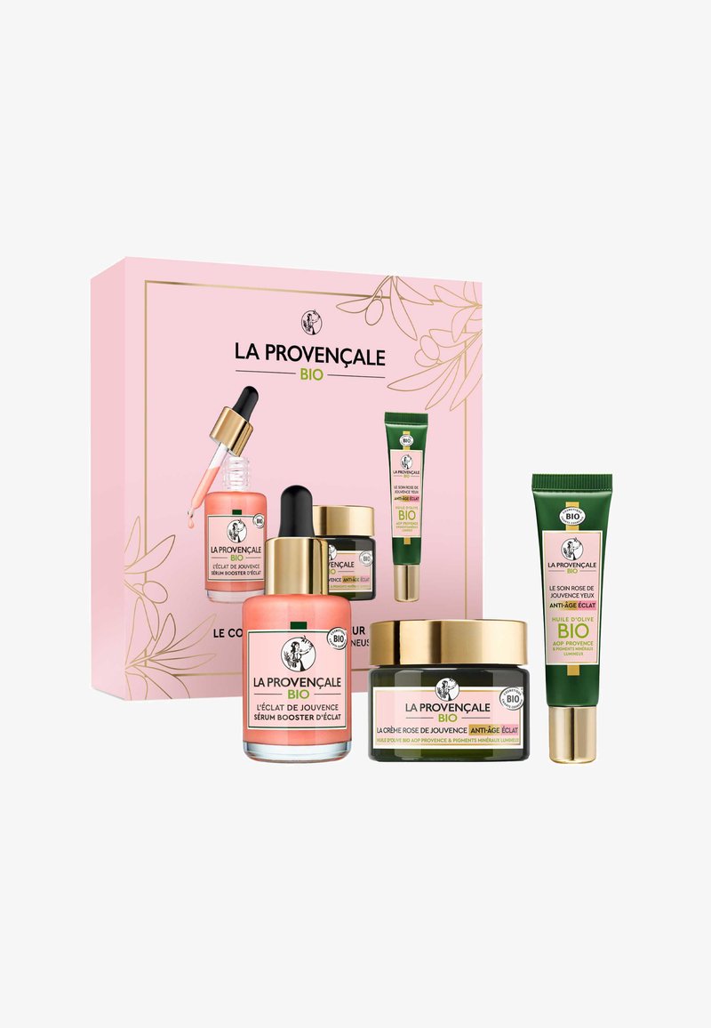 Ensemble de produits de soin de la peau dans une boîte rose. Comprend des bouteilles en verre avec des accents dorés, un pot de crème foncé et un tube vert. Différentes étiquettes visibles.