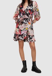 Robe portefeuille florale à manches longues, motifs rouge vif, rose et vert sur fond noir. Présente des volants superposés et une taille à nouer.