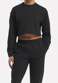 Černá zkrácená mikina s dlouhými rukávy, kulatým výstřihem a hladkým povrchem, v kombinaci s odpovídajícími černými tepláky se elastickým pasem.