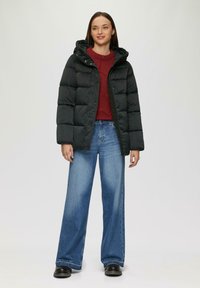 Schwarze Steppjacke mit Kapuze und abgestepptem Design. Worn über einem roten Pullover mit Rippen. Kombiniert mit weiten blauen Jeans und schwarzen Stiefeln.
