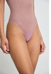 Light pink bodysuit with a textured pattern, high cut legs, and a smooth finish. Close-up of the shoulder and thigh area.