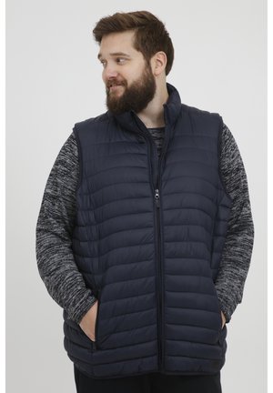 Chaleco acolchado de color azul marino con cuello alto y cierre de cremallera. Cuenta con bolsillos laterales y un diseño ligero con un patrón de acolchado vertical.