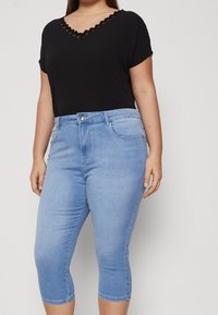 Černé tričko s krátkým rukávem a vroubkovaným výstřihem do V, spárované se světle modrými capri džíny s předním zapínáním na knoflík a bočními kapsami.