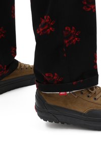 Baskets en daim marron et caoutchouc noir, avec des accents gris et une étiquette logo "VANS". Pantalon avec une base noire et un motif floral rouge.