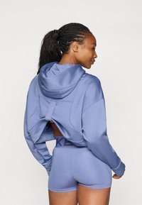 Felpa viola chiaro con design a schiena aperta, abbinata a pantaloni corti coordinati con un elastico brandizzato. Tessuto strutturato, vestibilità rilassata.