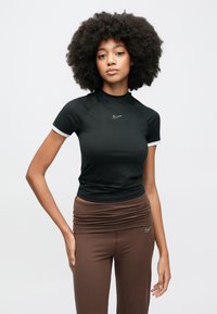 Fekete sportos felső rövid ujjal, fehér szegéllyel és Nike logóval. Barna, magas derekú leggingsszel párosítva, melynek derékrésze ráncolt.