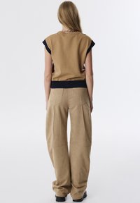 Beige gestricktes Oberteil mit kurzen Ärmeln und geripptem Saum, kombiniert mit weit geschnittenen, hellbraunen Wildlederhosen mit Vordertaschen und Nahtdetails.