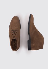 Chaussures en daim marron avec une texture lisse, dotées de bouts ronds et d'une semelle en caoutchouc noir bas; inclut des lacets pour un ajustement sécurisé.