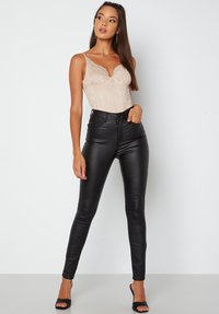 Svarta högmidjade skinny jeans i imitationläder som matchas med en nude lace bodysuit med justerbara remmar och vågiga kanter.